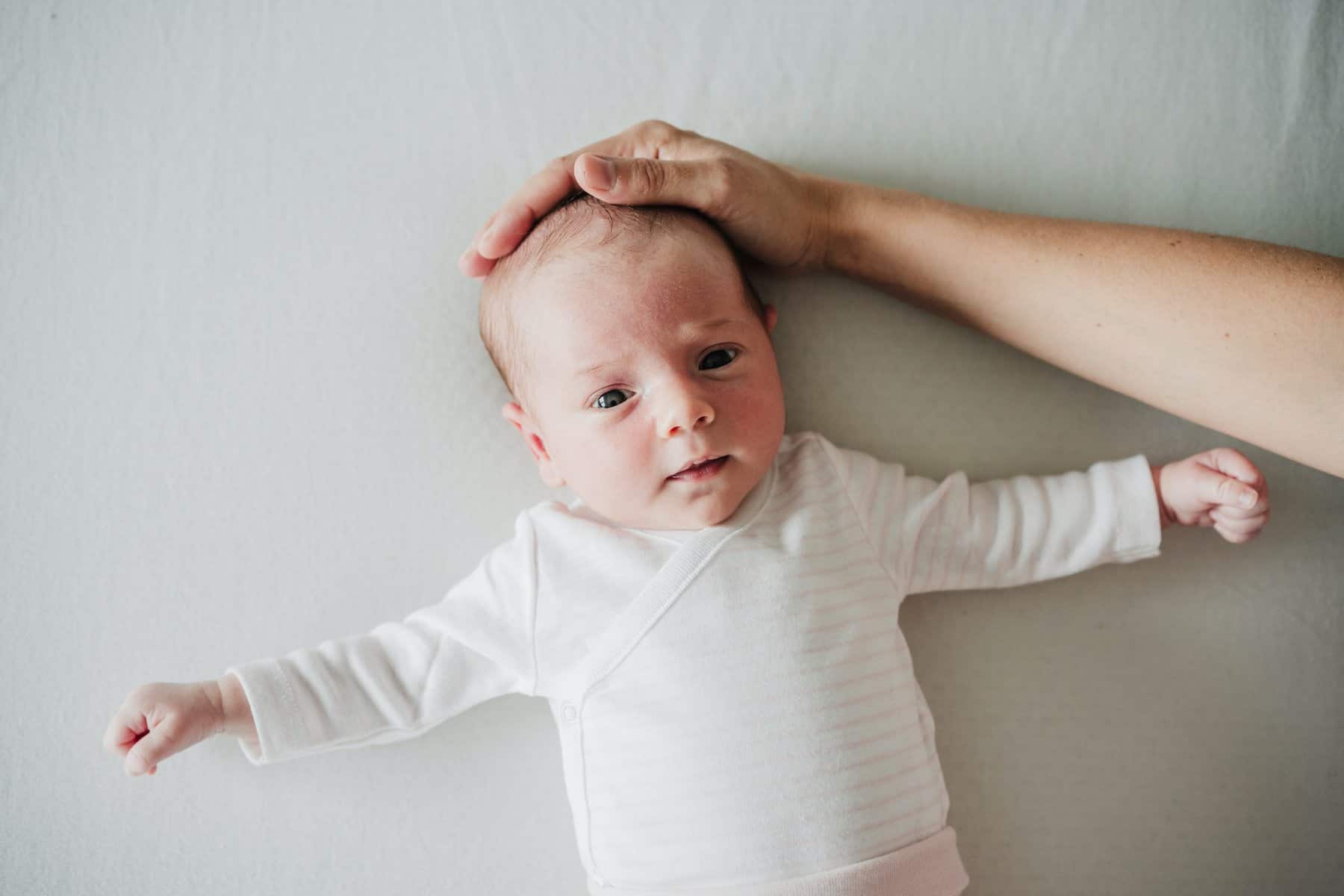 mother hand touching newborn baby head on bed at home.Family, love and protection concept